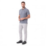 A man modeling a short-sleeve polo shirt in slate blue-gray with light gray trousers and black shoes, standing against a plain white studio background.