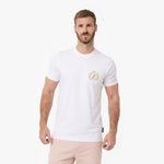 A man wearing a white T-shirt with a small gold and blue crest logo on the left chest