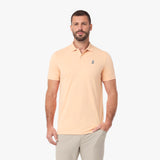 A man wearing a light peach-colored short-sleeve polo shirt with a small embroidered logo on the left chest
