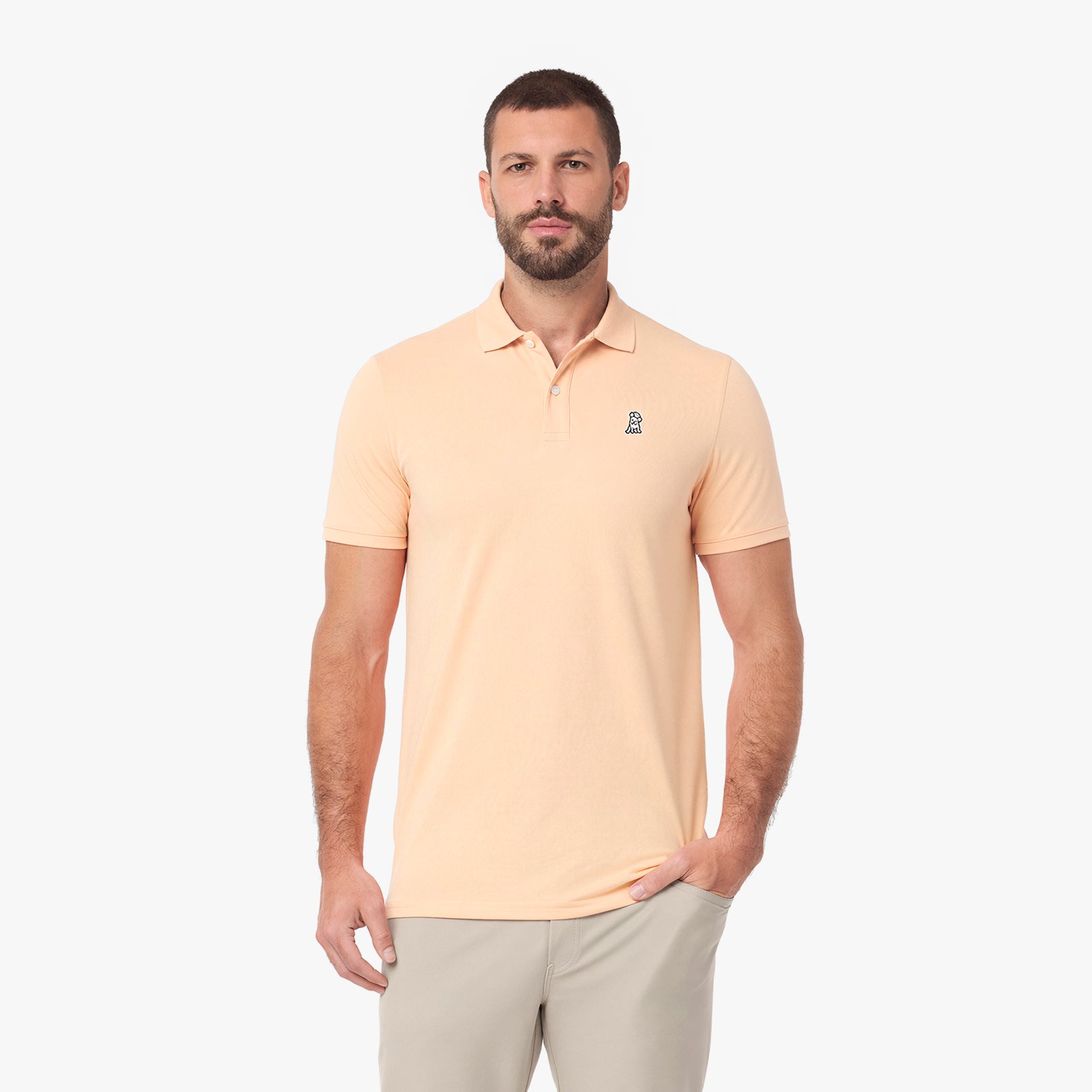 A man wearing a light peach-colored short-sleeve polo shirt with a small embroidered logo on the left chest