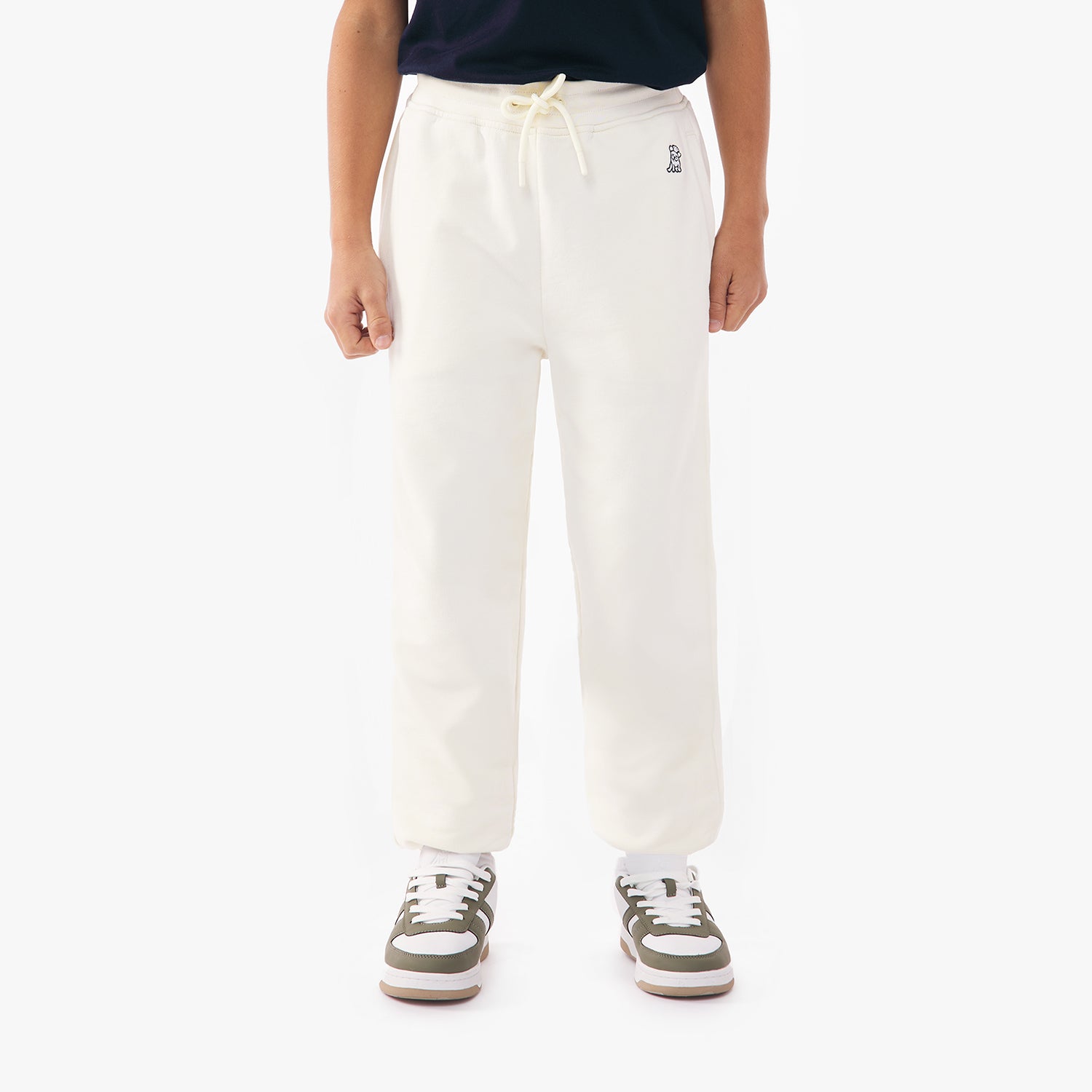 Front view of a child wearing off-white jogger pants with a drawstring waist, paired with green and white sneakers and a green top