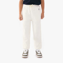 Front view of a child wearing off-white jogger pants with a drawstring waist, paired with green and white sneakers and a green top