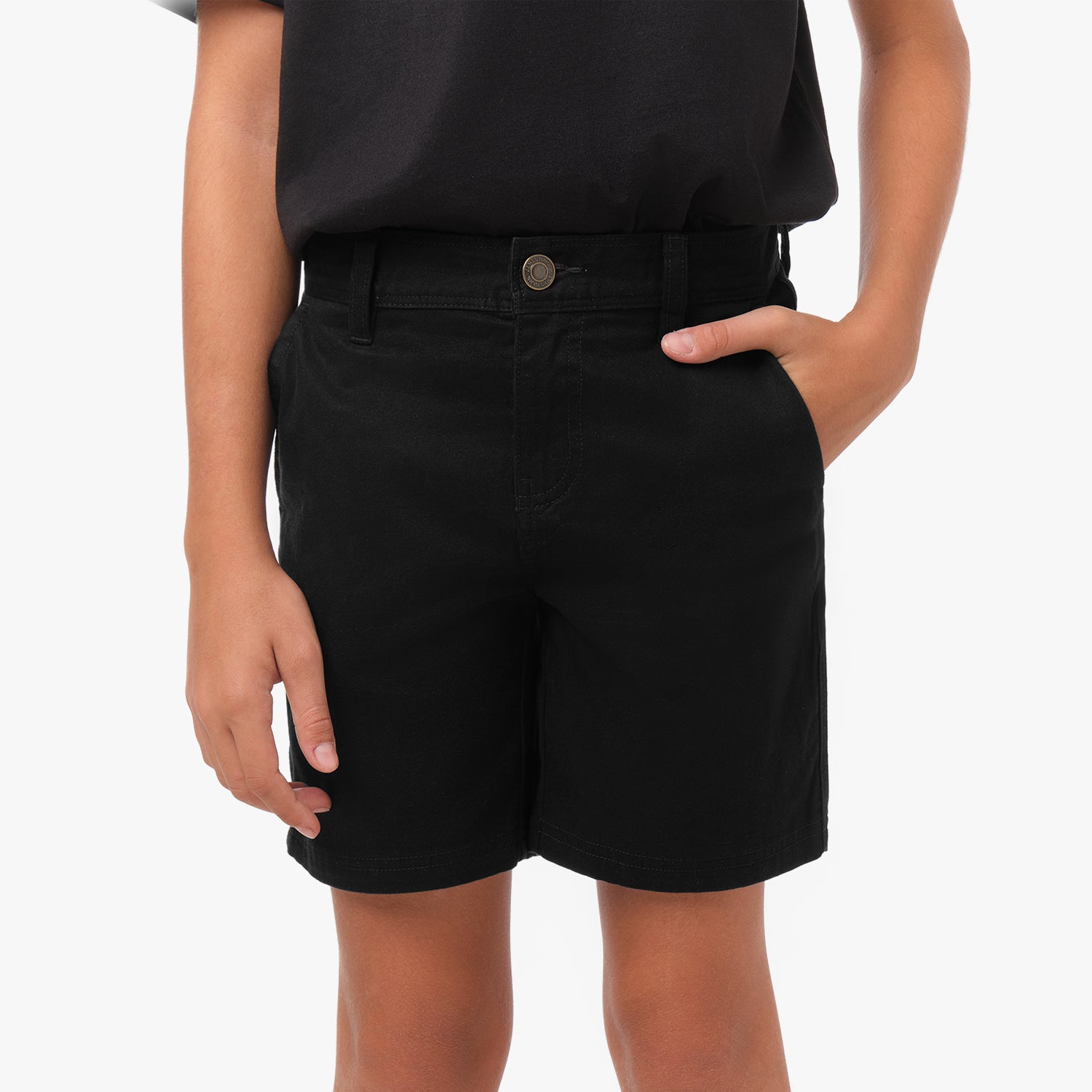 Close-up front view, waist-down, of a boy wearing black chino shorts with a black t-shirt. One hand is in the front side pocket. The shorts feature a button closure, belt loops, and fly