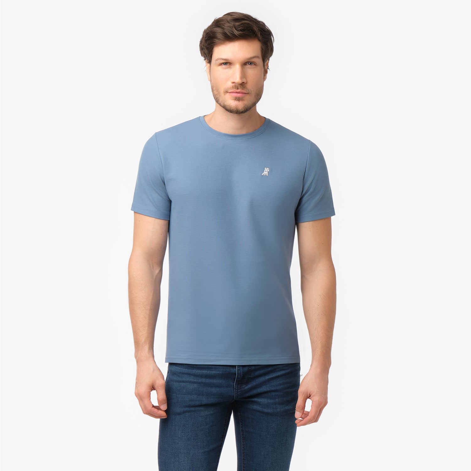 Male model showcasing the front of a light blue men's crew neck t-shirt with a logo, paired with dark blue denim jeans, shot on white.