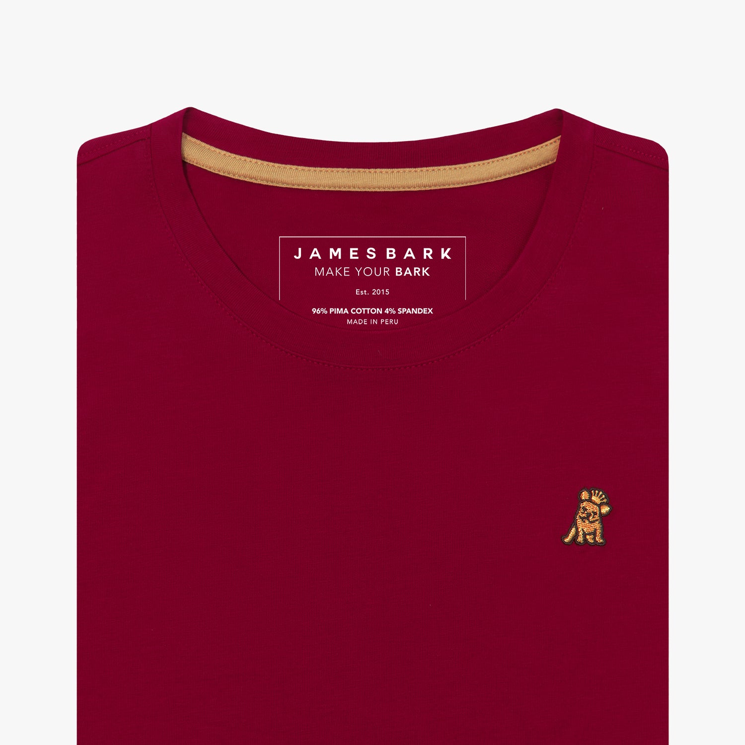 Detailed close-up view of a maroon women's crew neck t-shirt. Shows the printed internal brand tag "JAMES BARK", contrasting gold neck tape, and the gold/yellow embroidered dog logo just below the neckline on the left chest