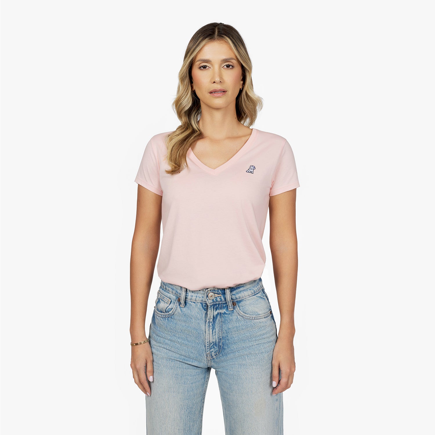 Front waist-up view of a female model wearing a light pink v-neck t-shirt with a small blue embroidered logo on the left chest, paired with light wash jeans