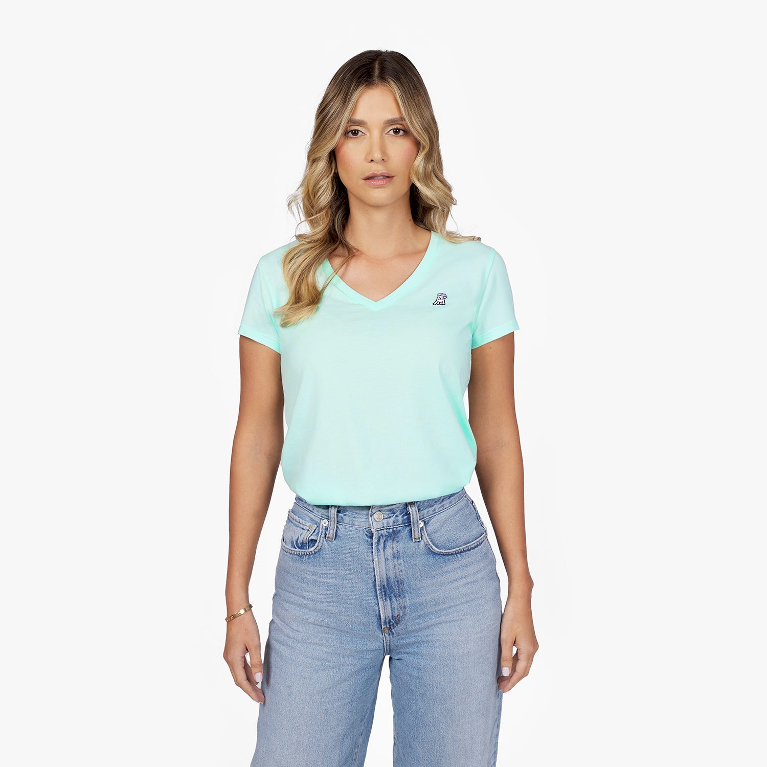 Front waist-up view of a female model wearing a mint green v-neck t-shirt with a small white embroidered logo on the left chest, paired with light wash jeans