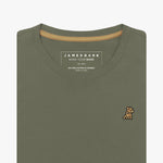 Detailed close-up view of an olive green women's crew neck t-shirt. Shows the printed internal brand tag "JAMES BARK", contrasting gold neck tape, and the gold/yellow embroidered dog logo just below the neckline on the left chest