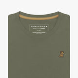 Detailed close-up view of an olive green women's crew neck t-shirt. Shows the printed internal brand tag "JAMES BARK", contrasting gold neck tape, and the gold/yellow embroidered dog logo just below the neckline on the left chest