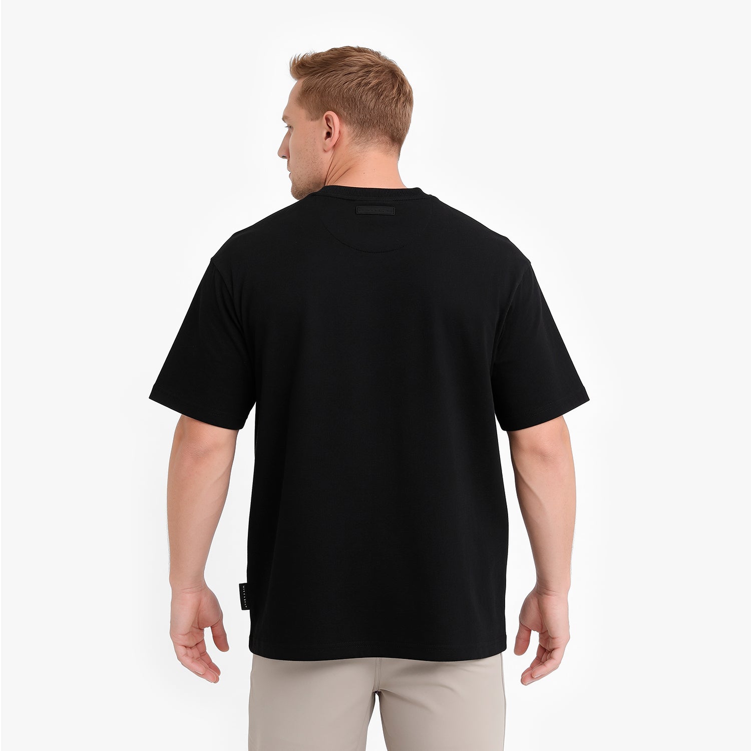 A man viewed from the back wearing a plain black t-shirt and light beige trousers