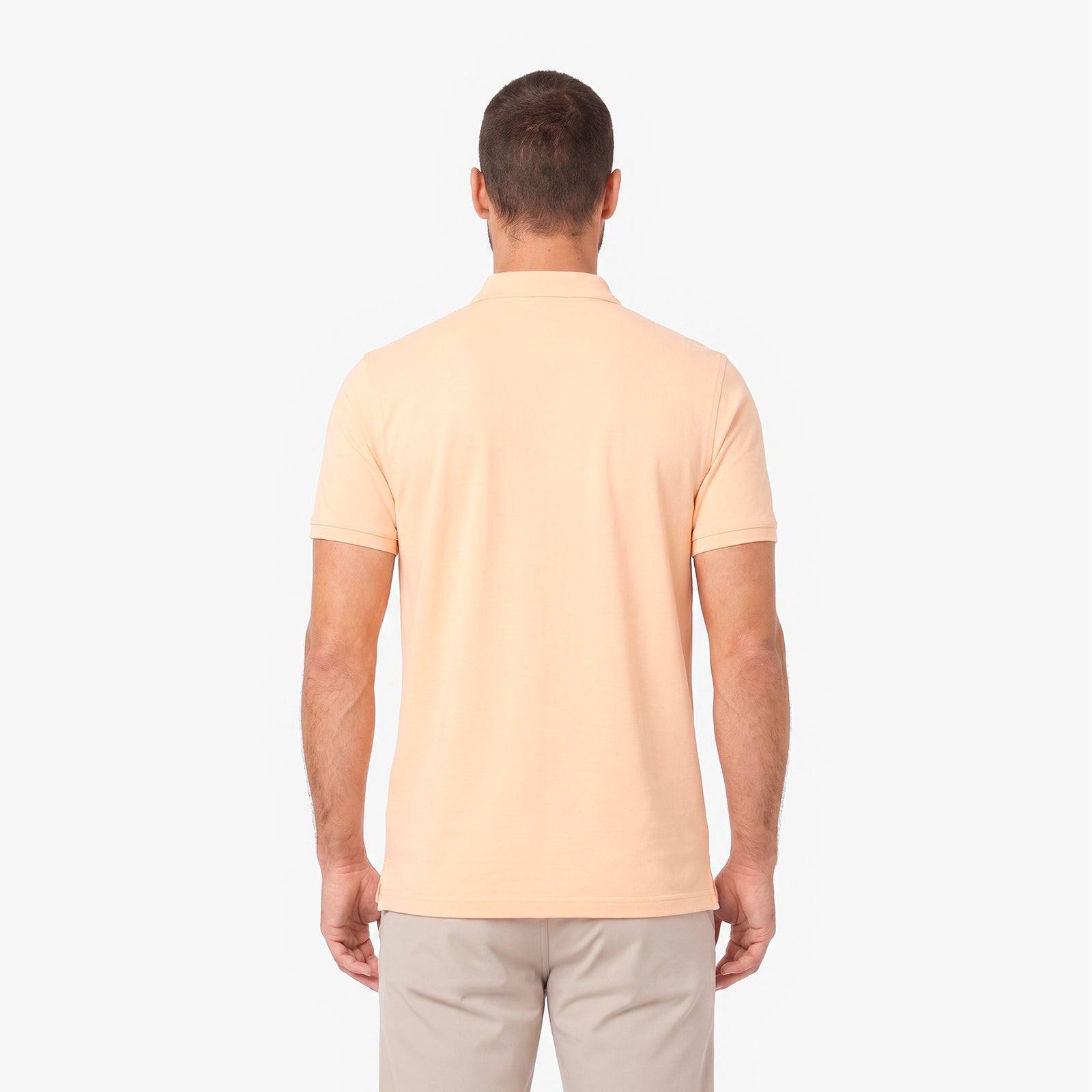 A man viewed from the back wearing a light peach-colored short-sleeve polo shirt and beige trousers