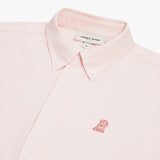 Close-up of the collar and upper chest area of a light pink button-down shirt. Features include a button-down collar, matching pink buttons, a beige "JAMES BARK" brand tag, and a tonal pink embroidered dog logo on the left chest