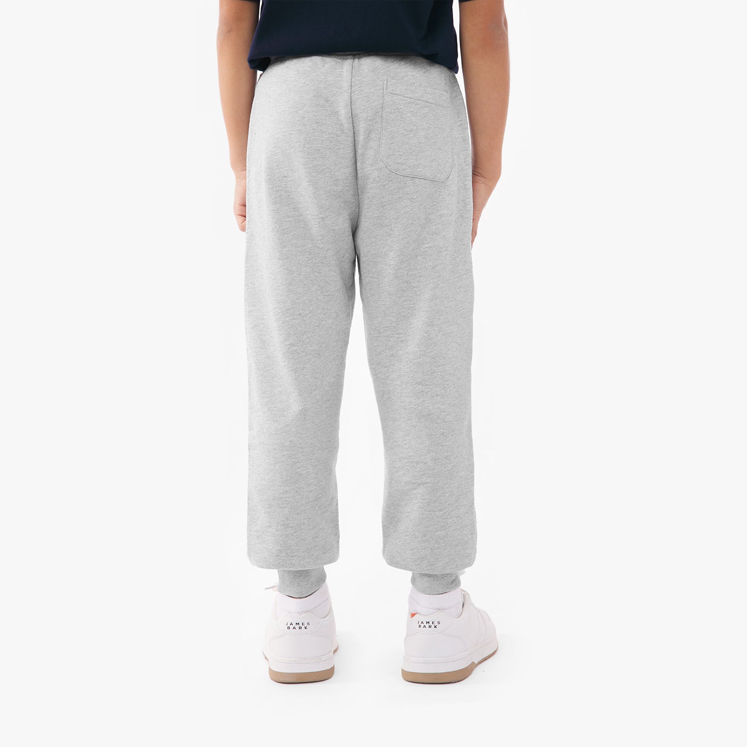 Back view of a person wearing light gray sweatpants with a single back pocket, paired with olive green and white sneakers, against a plain white background.