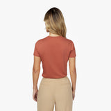 Back waist-up view of a female model wearing a plain rust-colored short-sleeve t-shirt tucked into beige trousers