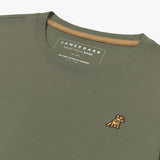 Close-up angled view of the inside collar area of the olive green crew neck t-shirt laid flat. Shows the ribbed neckline, gold neck tape, the printed "JAMES BARK" brand tag, and the gold/yellow embroidered dog logo on the chest