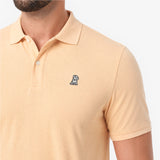 A close-up of a man wearing a light beige polo shirt with a small embroidered dog logo on the chest