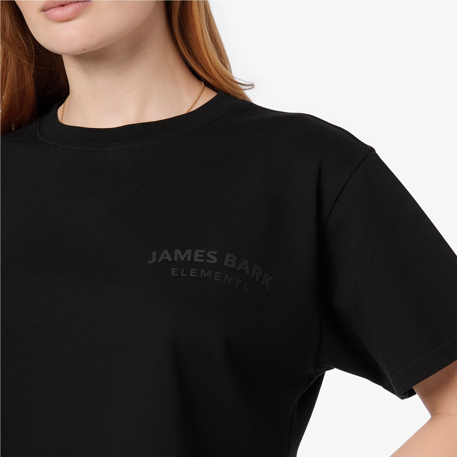 Close-up of the black 'James Bark Elements' logo printed on a black cotton cropped t-shirt.