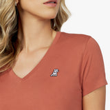 Close-up detail of the rust-colored v-neck t-shirt neckline, showing the fabric texture and the small white embroidered dog logo on the left chest