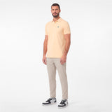 A man modeling a pale yellow polo shirt with beige trousers and black-and-white sneakers, standing against a plain white studio background.