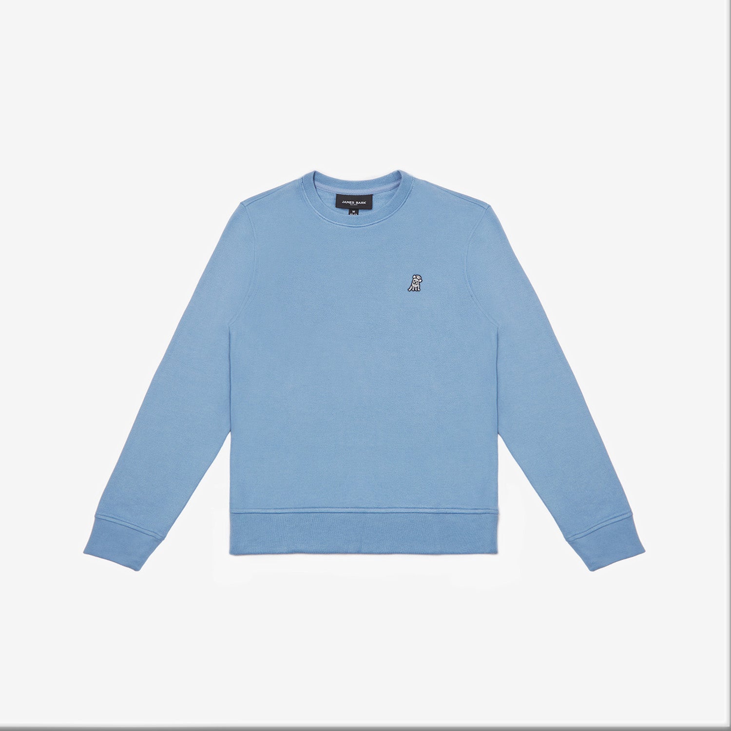 A light blue crewneck sweatshirt laid flat on a white background. It has long sleeves, ribbed cuffs, and a ribbed hem. A small embroidered logo of a dog is positioned on the left chest area. The neckline features a black label with white text. The fabric appears to be soft and comfortable