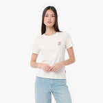 A woman modeling a T-shirt in off-white, featuring a small circular graphic on the left chest, paired with light blue jeans