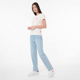 A woman modeling a white short-sleeve T-shirt with a small chest graphic, paired with light-wash blue jeans and white sneakers