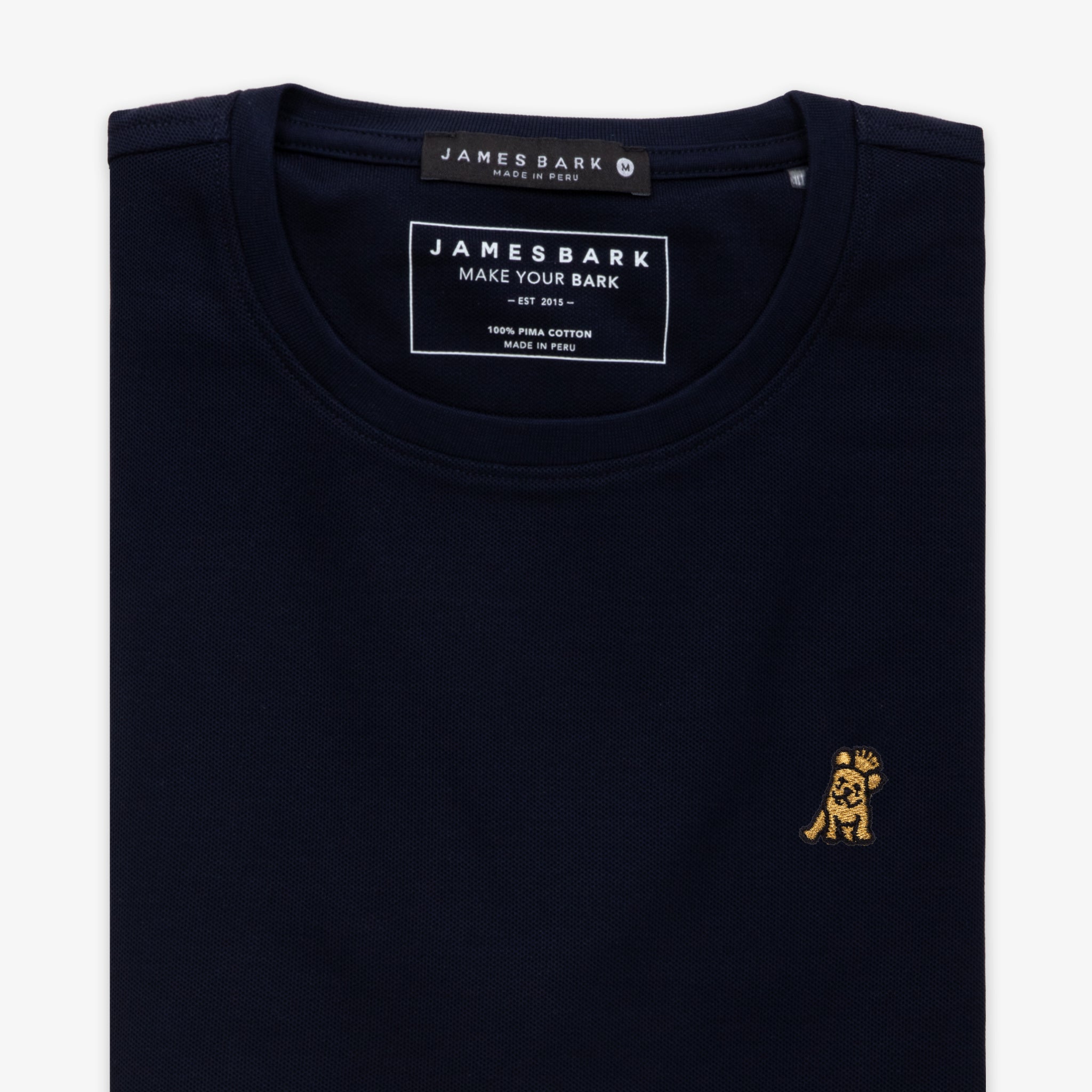 Close-up of the neckline of a navy blue T-shirt, showing the small golden embroidered logo on the chest and internal tag.