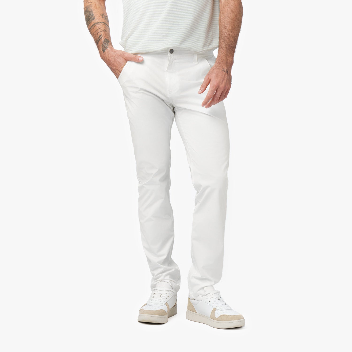 A close-up of a man wearing white pants, paired with white sneakers. The image focuses on the front of the pants, showing a slim, tailored fit with his hands in the pockets.