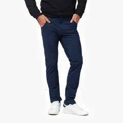 A close-up of a man wearing navy blue pants, paired with a black sweater and white sneakers. The image focuses on the front of the pants, showing a slim, tailored fit with his hands in the pockets.