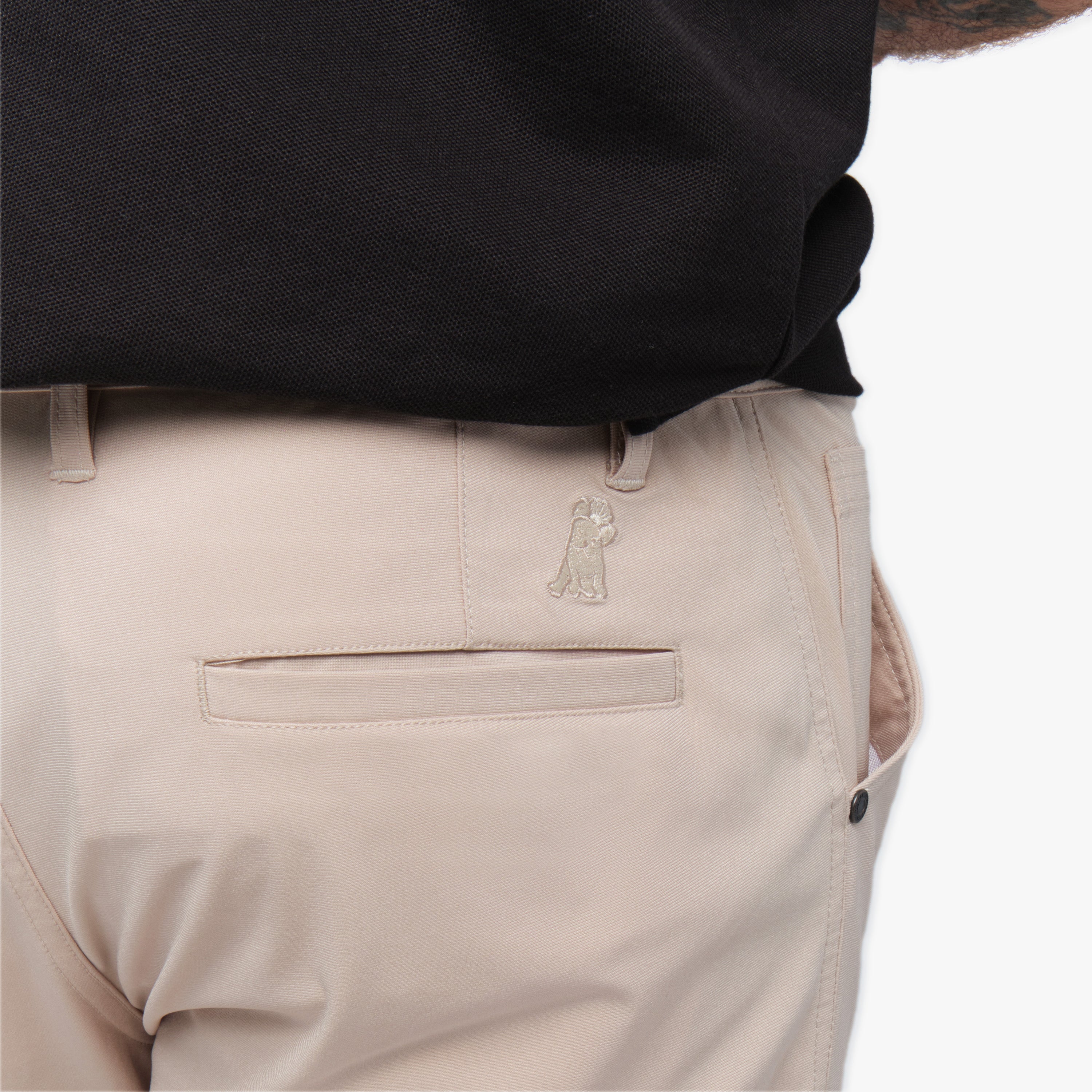 A close-up of the back pocket area of the beige pants, highlighting the subtle embroidered logo near the pocket.