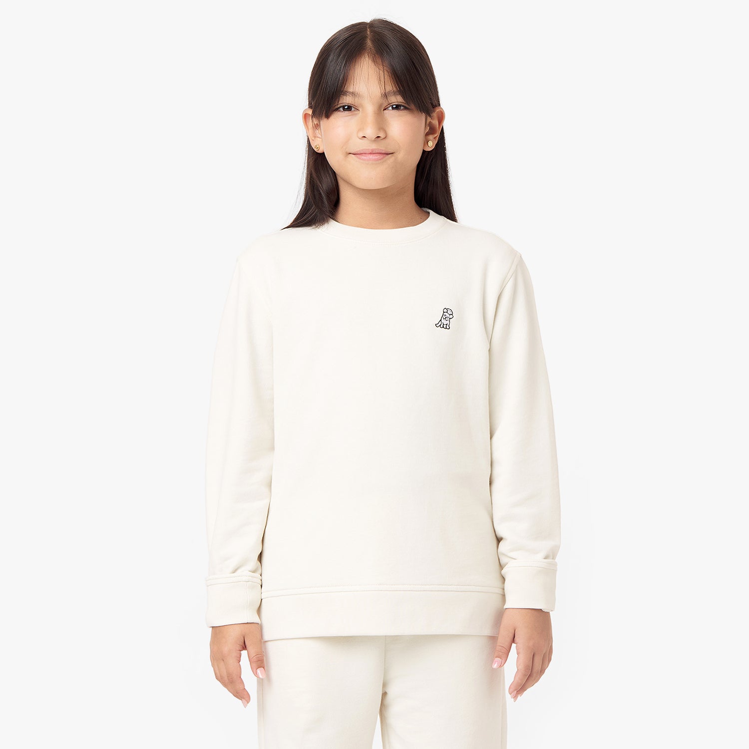 Front view of a child wearing a cream-colored sweatshirt with a small embroidered dog logo on the chest, paired with matching pants, standing confidently