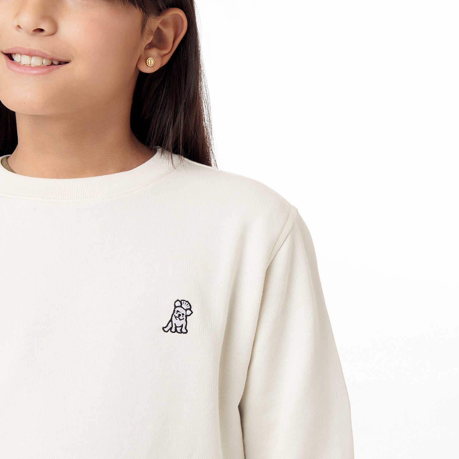 Side view of the child wearing the cream-colored sweatshirt, focusing on the chest area with the embroidered dog logo