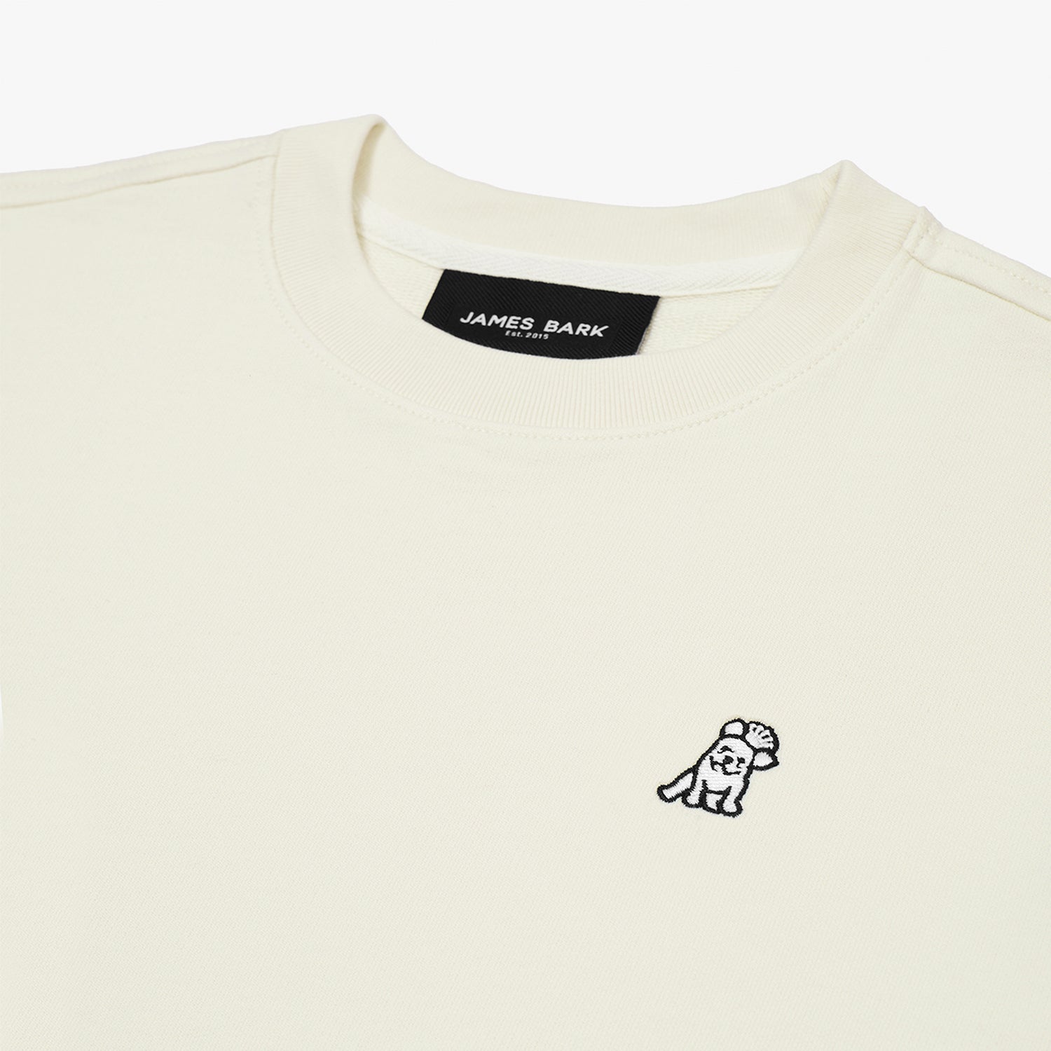 Close-up of the neckline and embroidered dog logo on the cream-colored sweatshirt, showcasing the fabric texture and details