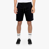 This image highlights black athletic shorts paired with white socks and black sneakers. The shorts have a clean design, featuring a drawstring waistband and a small embroidered logo on the leg. This outfit provides a sleek, sporty look ideal for both active and casual settings.