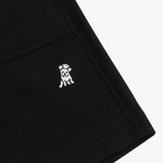 Close-up of a black fabric garment, highlighting a small embroidered white dog logo on the lower side. The stitching details are visible, showing a clean and structured design. The texture of the fabric appears to be a breathable, durable material, and the hem is neatly stitched.