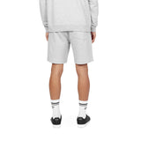 This image highlights the back view of the gray athletic shorts. The shorts feature a single back pocket on the right side, providing a minimalist and practical design. The model pairs the shorts with a matching gray sweatshirt and completes the look with white socks (featuring black stripes and branding details) and black sneakers, creating a cohesive and sporty outfit.