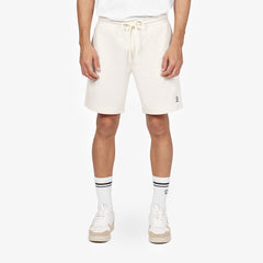 A close-up shot showcasing a model wearing off-white casual shorts with a drawstring waistband. The shorts are paired with white mid-calf socks featuring black stripes and white sneakers with beige soles, creating a clean and sporty aesthetic. The outfit emphasizes comfort and style with minimalist details