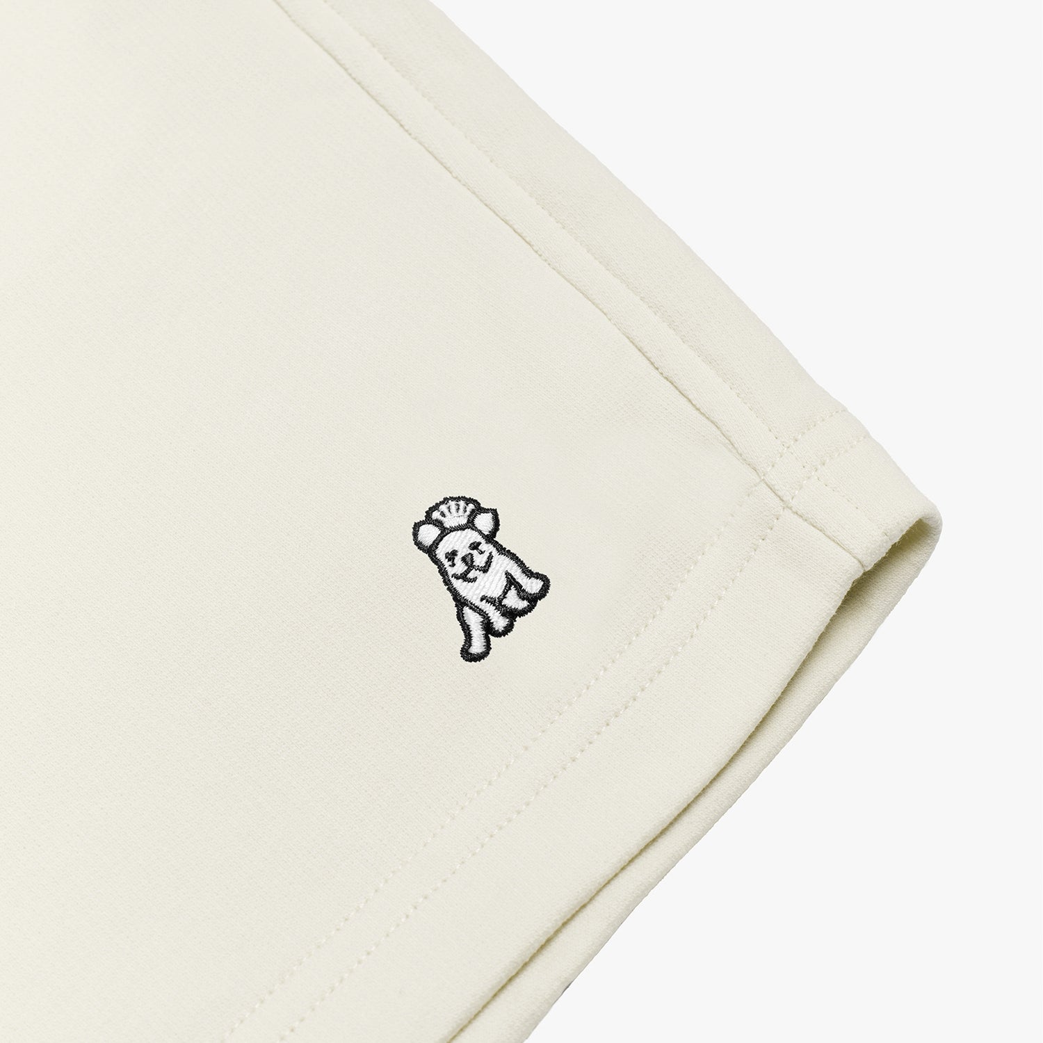 Close-up of the embroidered dog logo on the cream-colored shorts, highlighting the detailed stitching