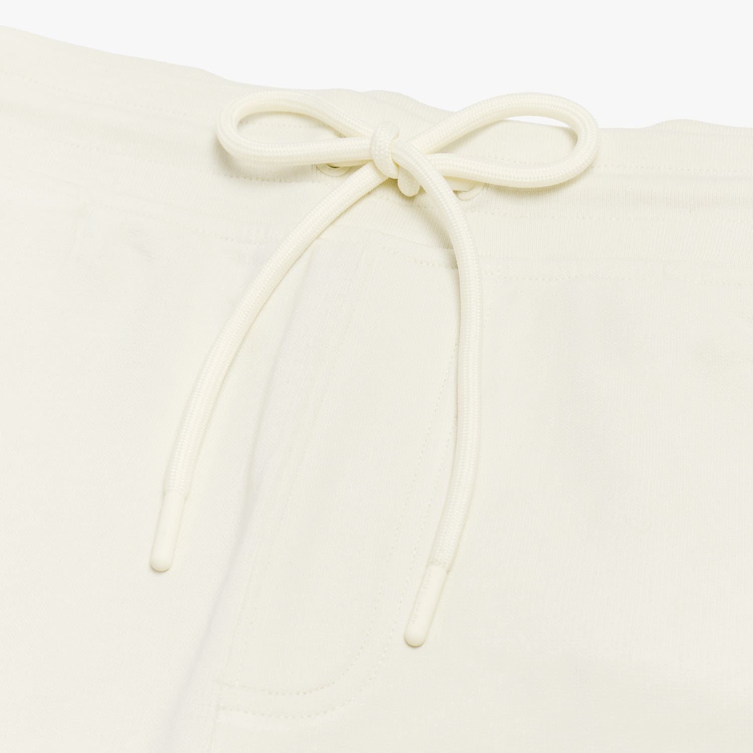 Close-up of the drawstring waistband on the cream-colored shorts, emphasizing the adjustable fit and fabric texture