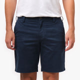 Close-up front view, waist-down, of a man wearing navy blue chino shorts with a white t-shirt. The shorts' button closure, belt loops, and front pockets are visible, with his hands down at his sides