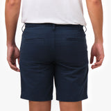 Close-up back view, waist-down, of a man wearing navy blue chino shorts with a white t-shirt, showing the two back welt pockets, belt loops, and the tonal embroidered logo