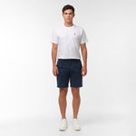 Full body shot of a man standing facing forward, wearing navy blue chino shorts, a white t-shirt with a logo, and white sneakers