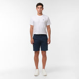 Full body shot of a man standing facing forward, wearing navy blue chino shorts, a white t-shirt with a logo, and white sneakers