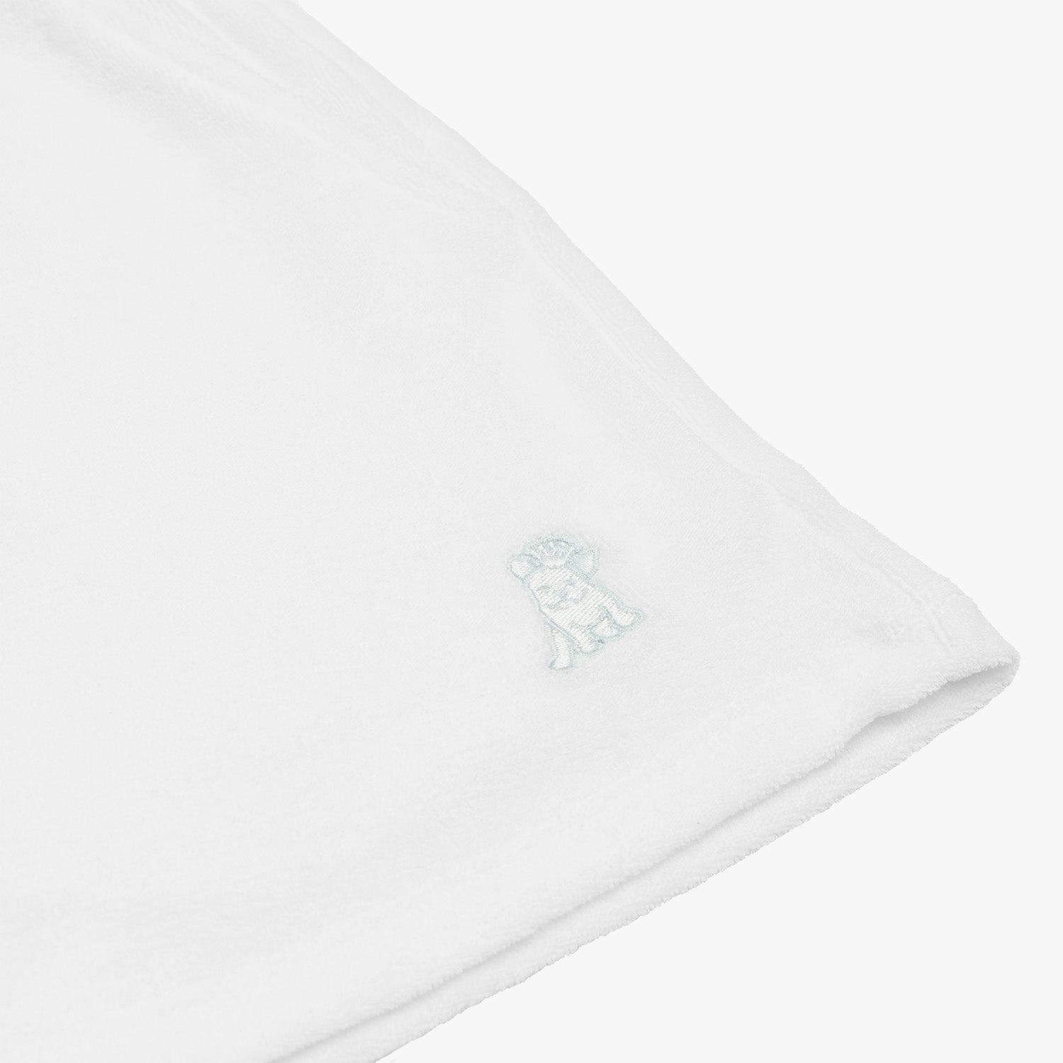 Close-up of the hem of white shorts, featuring a subtle embroidered dog logo in light blue, highlighting the fine details and minimalistic design