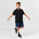 Full-body shot of the boy wearing the black polo shirt paired with navy blue shorts, walking with his arms outstretched.