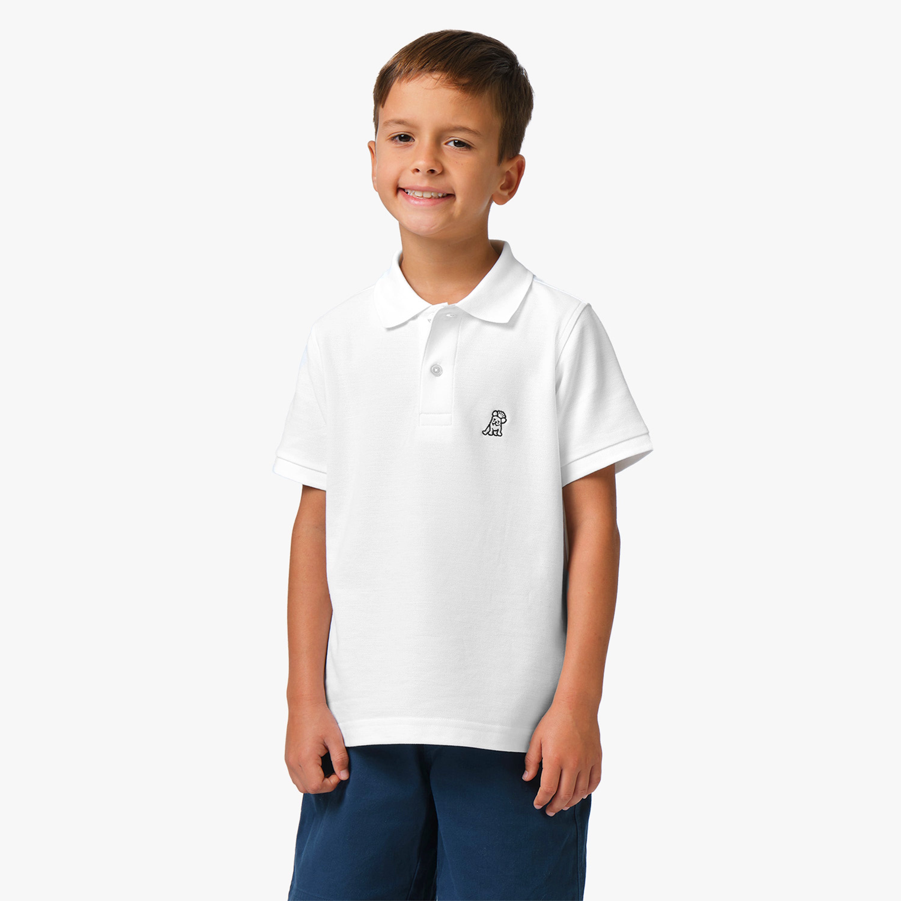 A young boy wearing a white polo shirt with a small embroidered logo on the chest, standing and smiling.