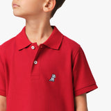 Close-up of the chest area of the red polo shirt, featuring the small embroidered logo.