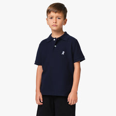 A young boy wearing a navy blue polo shirt with a small embroidered logo on the chest, standing with his hands at his sides.