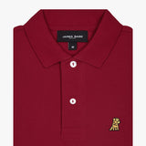 Close-up of the collar and upper part of the red polo shirt, showing the buttons and the small golden embroidered logo on the chest.