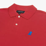 Detailed close-up of the blue embroidered dog logo on a red polo shirt